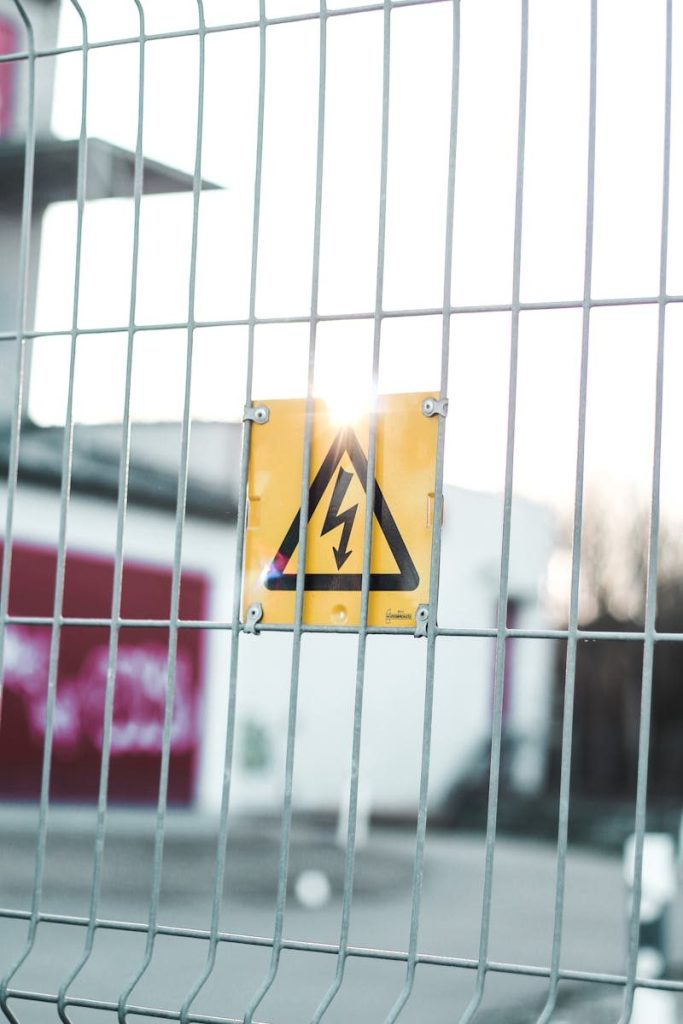 Yellow high voltage sign mounted on a metal fence, indicating caution and safety in an urban area.